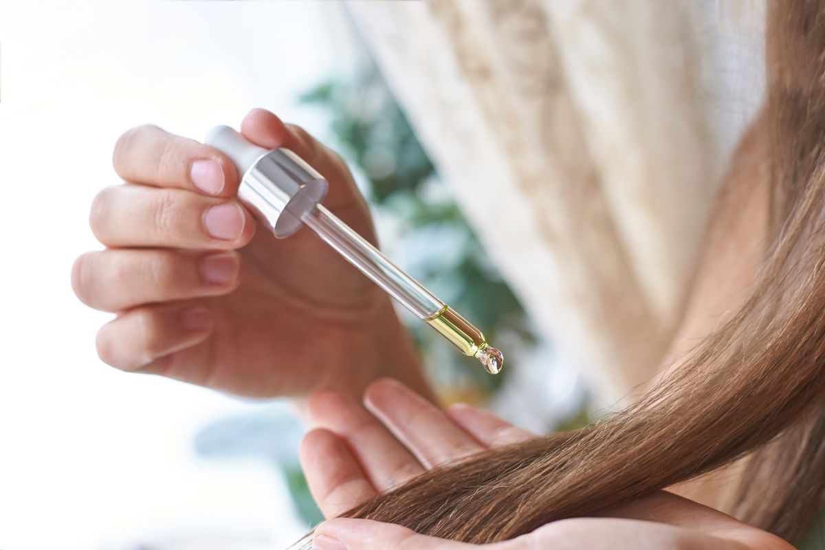 Hands using a dropper to put oil on hair.